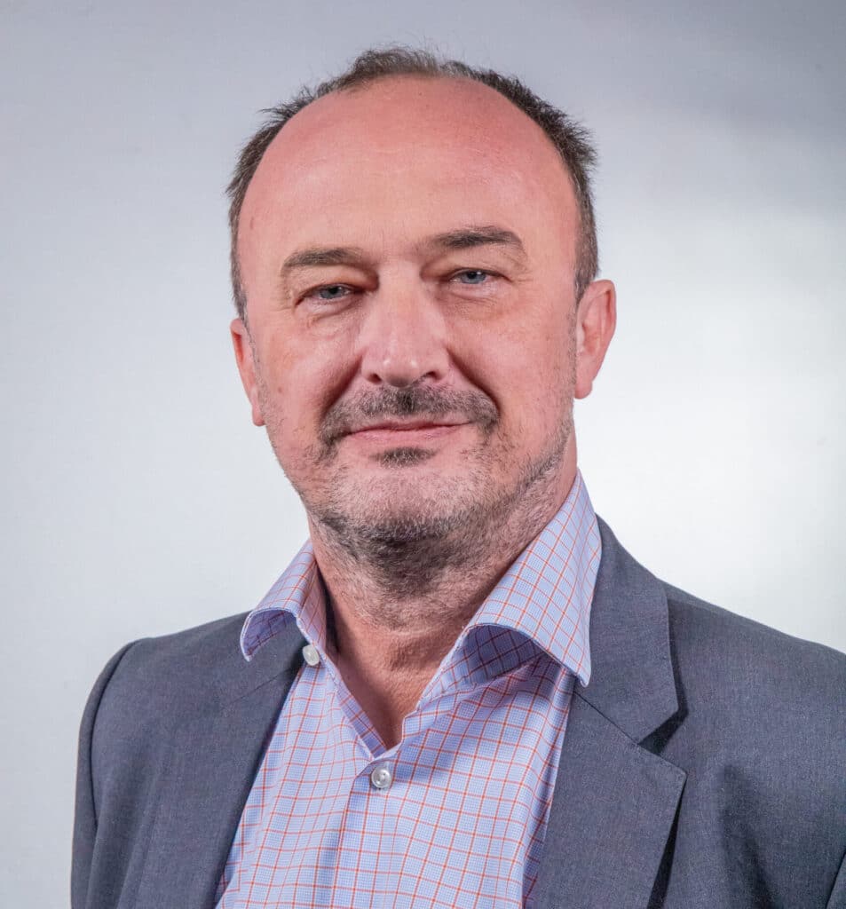 Portrait de Frédéric Chevalier, Directeur Général ENSIO Groupe et Directeur Contrat Orange, veste grise et chemise à carreaux bleu et rouge sur fond gris clair