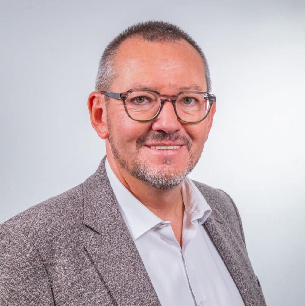 Portrait de Frédéric Demey, Groupe ENSIO, veste grise et chemise blanche sur fond gris clair