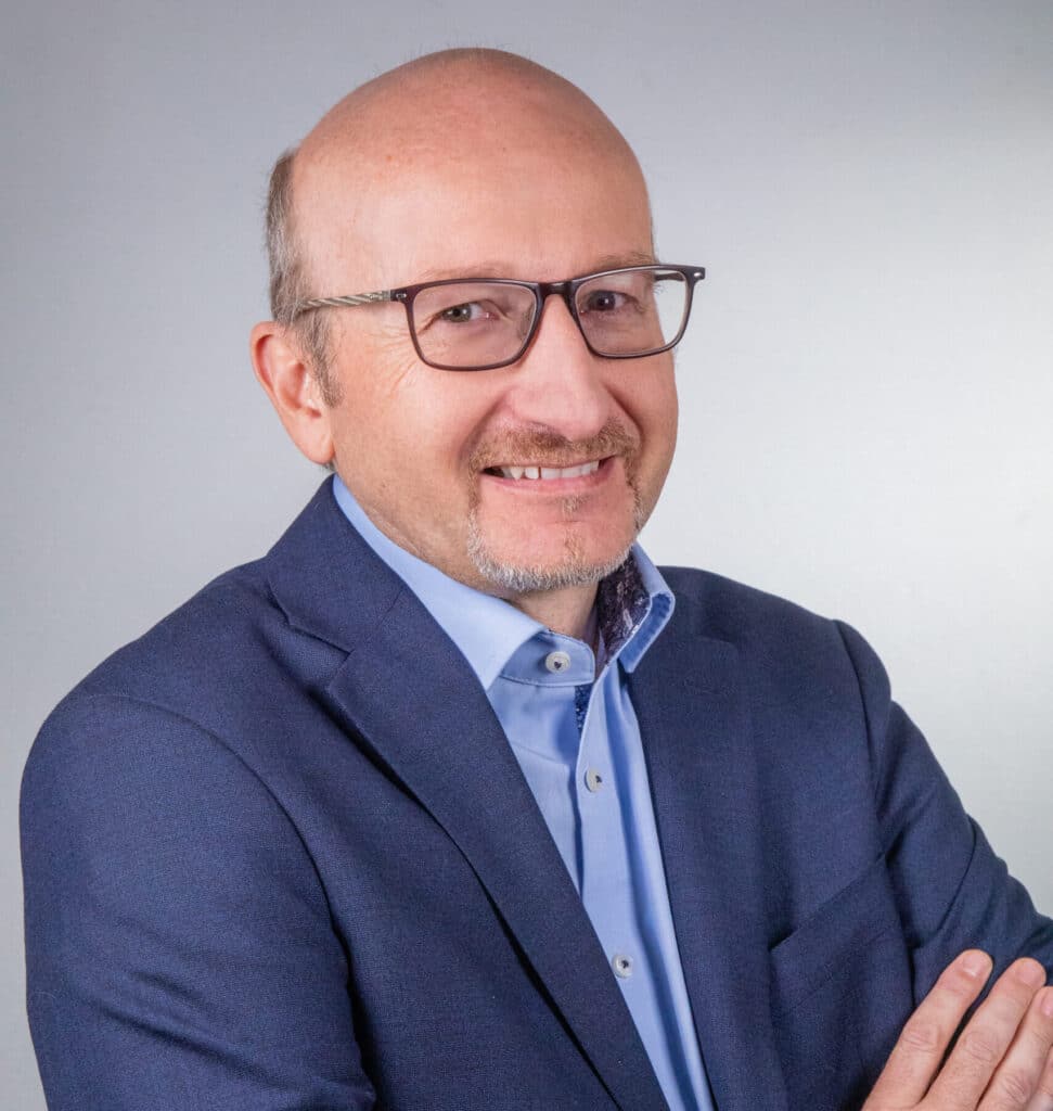 Portrait d'Olivier Lopez, Président du Groupe ENSIO, veste bleu marine et bras croisés sur fond gris clair
