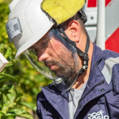 Technicien ENSIO en combinaison bleue et casque avec visière de protection raccordant un câble électrique lors d'un branchement sur le réseau